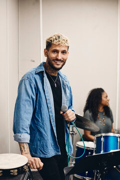 Portrait of smiling young artist holding microphone standing in classroom