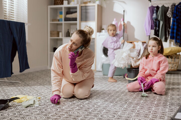 A woman cleans house with young daughters. A girl talking on the phone with a telemarketer, friend, husband. A busy mom scrubs the bathroom floor with a brush.