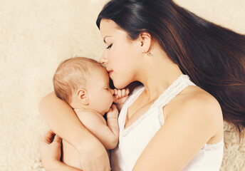 Portrait of mother with sleeping baby lying on the bed together at home
