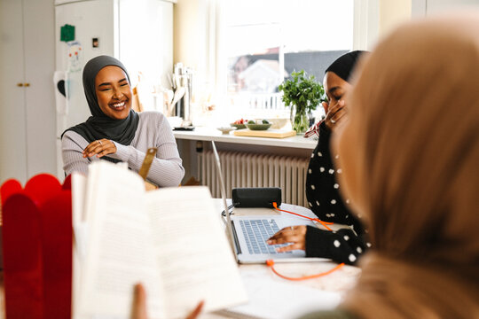 Cheerful young woman wearing hijab sitting with friends at table