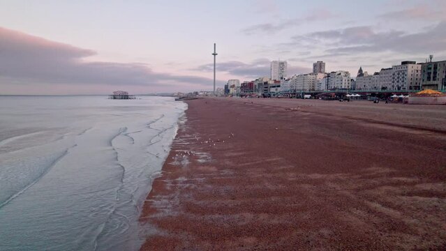 Drone rises backwards from quiet beach to reveal Brighton and British Airways i360 at dawn in UK