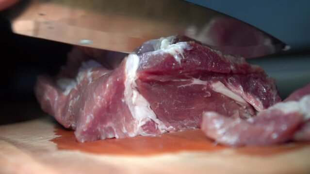 Close-up of hands of woman, housewife, preparing dish of meat. Girl's hands cut raw pork meat with knife for further cooking. Meat-eating. Cutting board, kitchen. Homemade dish. slow motion