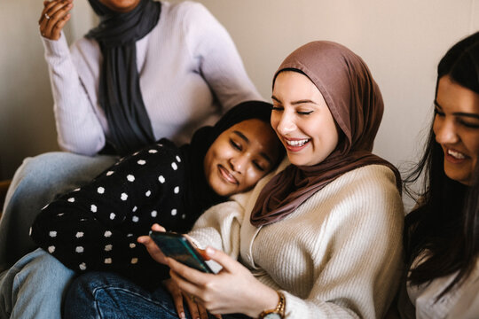 Smiling woman leaning on female friends using smart phone at home