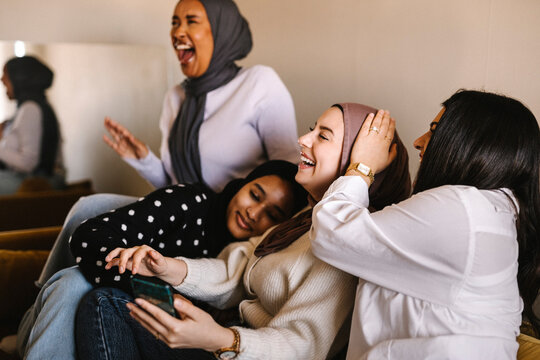 Young women laughing while sitting together on sofa at home