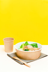 Healthy food lunch in kraft paper carton eco friendly box disposable bowl packaging container, cup on yellow background. chicken, eggs, greens. Take away delivery. environment protection, vertical