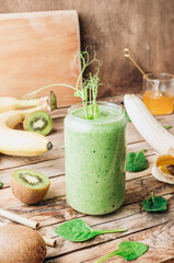 Green healthy smoothie in glass with banana, kiwi and spinach on rustic wooden background