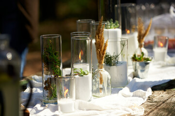Wedding party banquet outdoors in forest. Dining table decorated in boho style with candles, white cloth, flowers, served with plates, tableware, dishes, meals, stemware and drinks. Holiday catering.