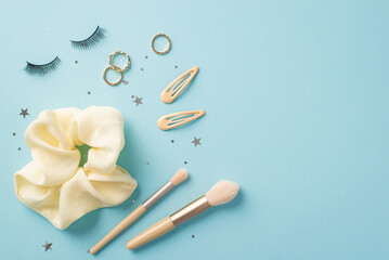 Make up concept. Top view photo of scrunchy makeup brushes barrettes false eyelashes gold rings and star shaped confetti on isolated pastel blue background with empty space
