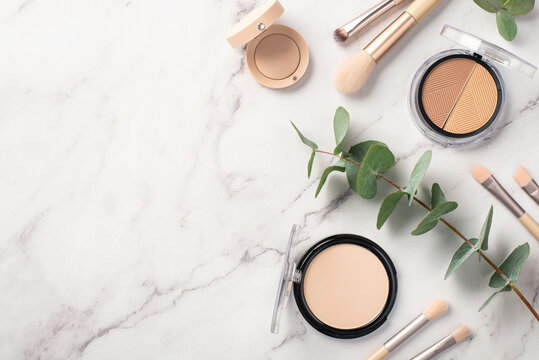 Make-up concept. Top view photo of makeup brushes contouring palette eyeshadow compact powder and eucalyptus on white marble background with empty space