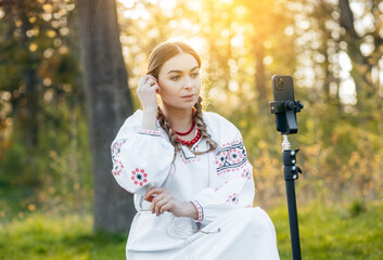 Ukrainian young blogger girl in national costume shooting some video on phone, while traveling in...