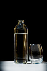  glass bottle with water and a glass tumbler, black background, concept of vitality, health, wellbeing