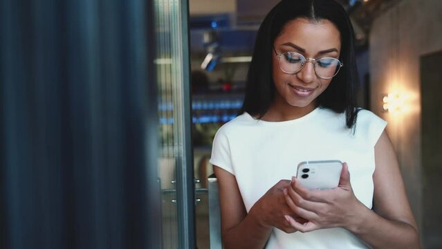 Positive African woman texting by mobile in cafe