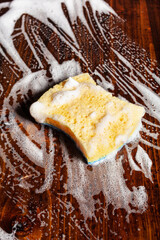 cleaning sponge wiping foam soap suds on wooden background, household washing concept