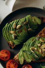 avocado toast with pumpkin seeds and cherry tomatoes close-up. sandwich with sliced green avocado slices top view 