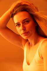 Natural beauty. Portrait of young beautiful woman barely smiling, posingisolated over orange studio background in neon.