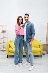 Fototapeta na wymiar Positive multiethnic couple holding key and looking at camera at home.