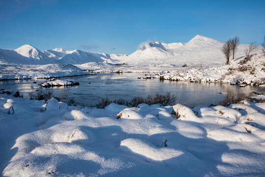Beautiful Winter landscape image looking towards Scottish Highlands mountain range across Loch Ba on Rannoch Moor