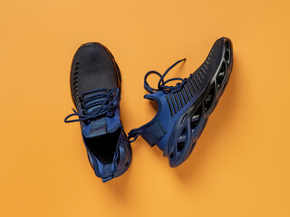 Laced up black blue mesh fabric sneakers over orange background. Pair of grooved men shoes for...