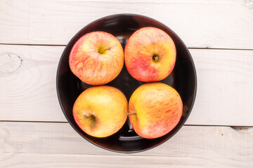Several red organic apples with a black ceramic plate on a wooden table, close-up, top view.