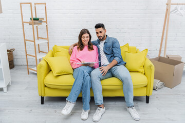 Smiling interracial couple holding color palette on couch at home.