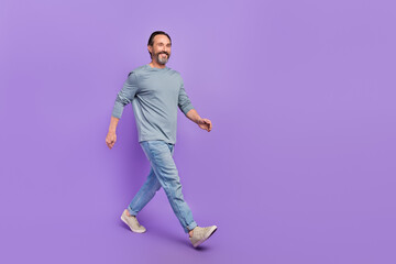 Full size profile portrait of satisfied adult person walking look empty space isolated on purple color background