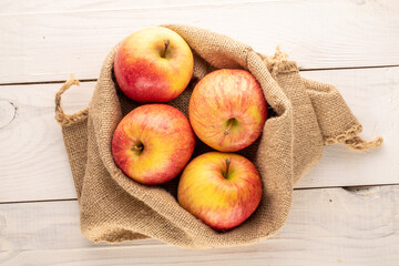 Several red organic apples in a jute bag on a wooden table, close-up, top view.