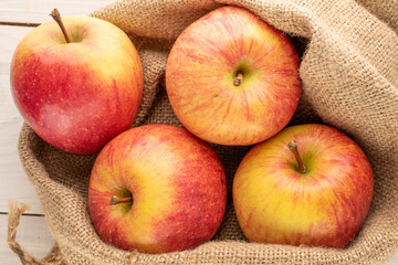 Several red organic apples in a jute bag on a wooden table, close-up, top view.