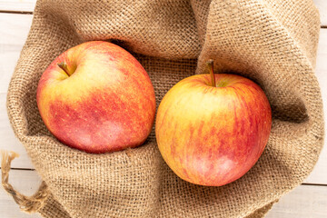 Two red organic apples in a jute bag on a wooden table, close-up, top view.