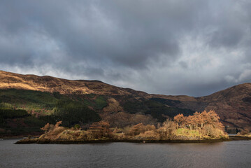 Stunning Winter landscape view along Loch Leven towards snowcapped mountains in distance with dramatic sky