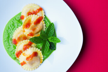 Italian pasta ravioli with burrata filling with tomato and pea cream on white plate shot from above with red background in horizontal shot