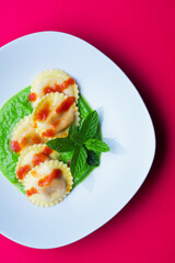 Italian pasta ravioli with burrata filling with tomato and pea cream on white plate shot from above with red background in vertical shot