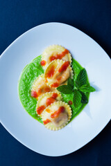 Italian pasta ravioli with burrata filling with tomato and pea cream on white plate shot from above with dark background in vertical shot