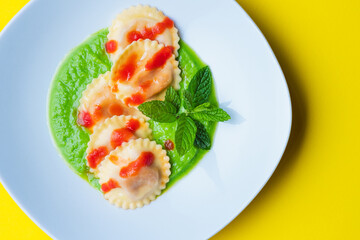 Italian pasta ravioli with burrata filling with tomato and pea cream on white plate shot from above with yellow background in horizontal shot