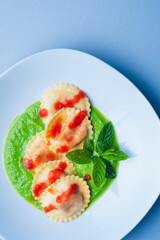 Italian pasta ravioli with burrata filling with tomato and pea cream on white plate shot from above with sky blue background in vertical shot