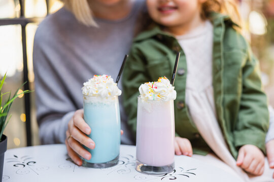 cropped view of blurred mother and daughter near glasses with milkshake and whipped cream.