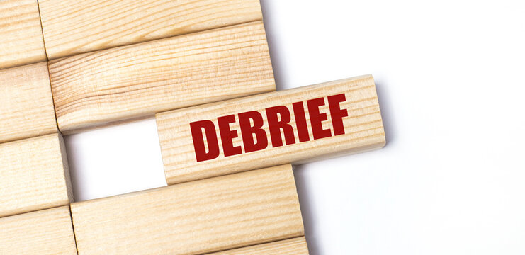 On a light background, wooden blocks with the text DEBRIEF. Close-up top view.
