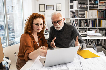 A senior designer helps his young female coworker to solve a problem.Design studio.	

