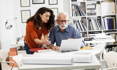 A senior designer helps his young female coworker to solve a problem.Design studio.	
