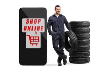 Full length portrait of an auto mechanic holding a tire and leaning on a smartphone with text shop...
