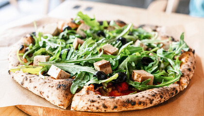 vegan pizza with arugula or rucola tofu olives and tomatoes close-up wooden board vegetarian food...