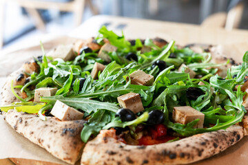 vegan pizza with arugula or rucola tofu olives and tomatoes close-up wooden board vegetarian food healthy eating