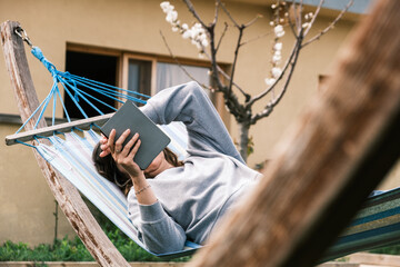 Mature woman in a hammock on a lawn on the lawn reading an e-book