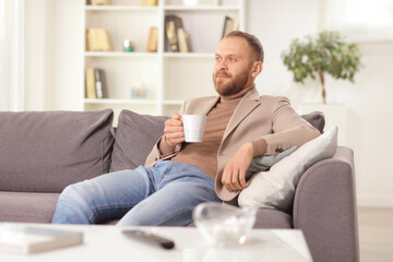 Man sitting on a sofa at home with a cup of tea and thinking