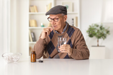 Elderly man at home taking a pill with a glass of water