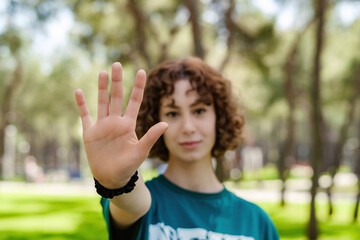 Young redhead woman wearing green tee doing stop sign with palm of the hand. Warning expression with negative and serious gesture on the face. Selective focus on her hand.