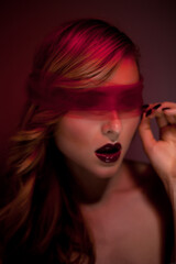 Sexy Blond Beauty Fashion Model with Sheer Red Blindfold and Red Light in a Dark Studio. Dominatrix Concept