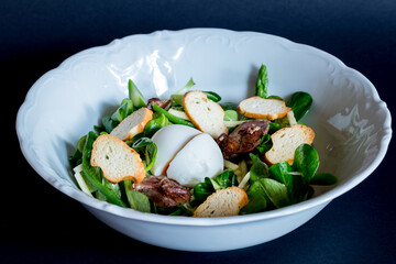 Salad with chicken liver and greens with poached egg on white bowl