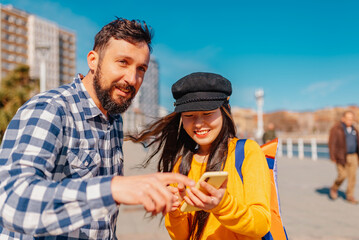 Asian young girl sightseeing and asking a Caucasian man for directions by pointing to a place on...