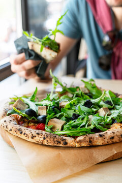 man eating vegan pizza with arugula or rucola tofu olives and tomatoes close-up wooden board vegetarian food healthy eating