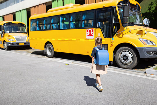 Back to school. Little girl from elementary school outdoor near yellow bus. Kid going learn new things 1th september